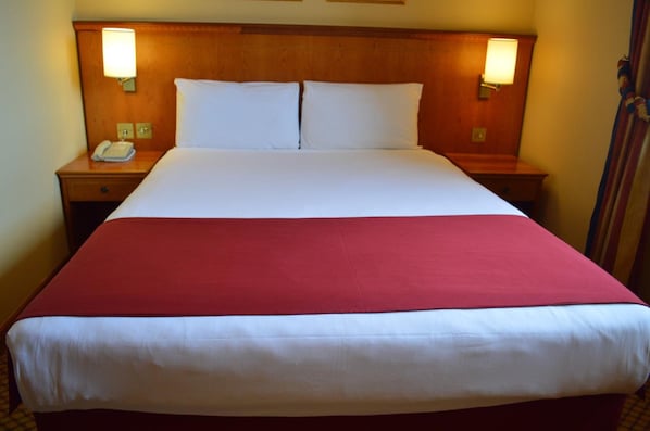 A hotel room with a large bed, two bedside tables, a telephone, and wall-mounted lamps.