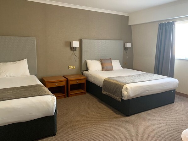 Habitación de hotel con dos camas, piso alfombrado y ventana con cortinas.