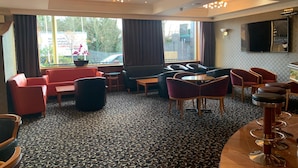 Een hotel lobby met een kamerbreed tapijt, zithoeken met rode en zwarte stoelen, een bank en een bar met krukken.
