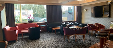 Eine Hotelhalle mit einem gemusterten Teppich, Sitzbereichen mit roten und schwarzen Stühlen, einem Sofa und einer Bar mit Hockern.