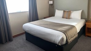 Een hotelkamer met een groot bed, een nachtkastje, een lamp en een raam met gordijnen.