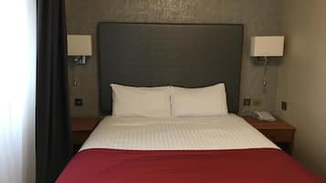 A hotel room with a large bed, two bedside lamps, a telephone, and a nightstand.