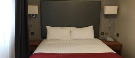 A hotel room with a large bed, two bedside lamps, a telephone, and a nightstand.