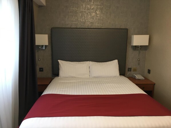 A hotel room with a large bed, two bedside lamps, a telephone, and a nightstand.