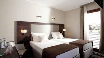 A hotel room with two beds, a desk with a chair, and a window with curtains.