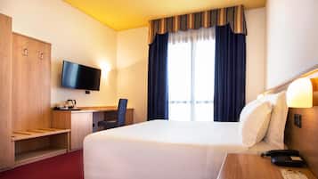 A hotel room with a large bed, a desk with a chair, a television, and a window with curtains.
