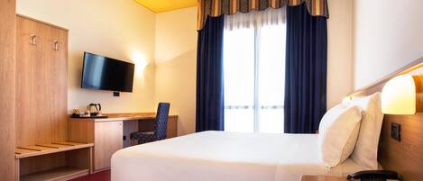 Habitación de hotel con una cama grande, un escritorio con silla, televisor y ventana con cortinas.