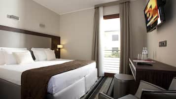 Habitación de hotel con una cama grande, un escritorio con una silla, un televisor y una ventana con cortinas.