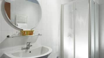 Ein Badezimmer mit einem weißen Waschbecken, einem Spiegel und einer Glasdusche.