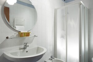 Un bagno con un lavandino bianco, uno specchio e un box doccia in vetro.