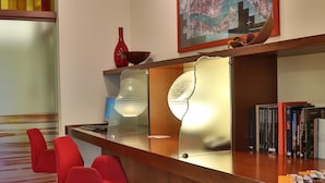Zona de recepción con mostrador de madera, sillas rojas, un mapa en la pared y una estantería con libros.
