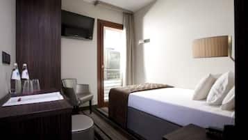 Ein Hotelzimmer mit Bett, Schreibtisch mit Stuhl, Wandfernseher und einem fenster mit Vorhängen.
