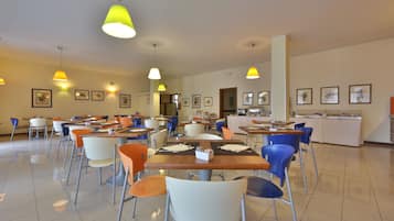 A spacious dining area with multiple tables and chairs, overhead lighting, and framed pictures on the walls.