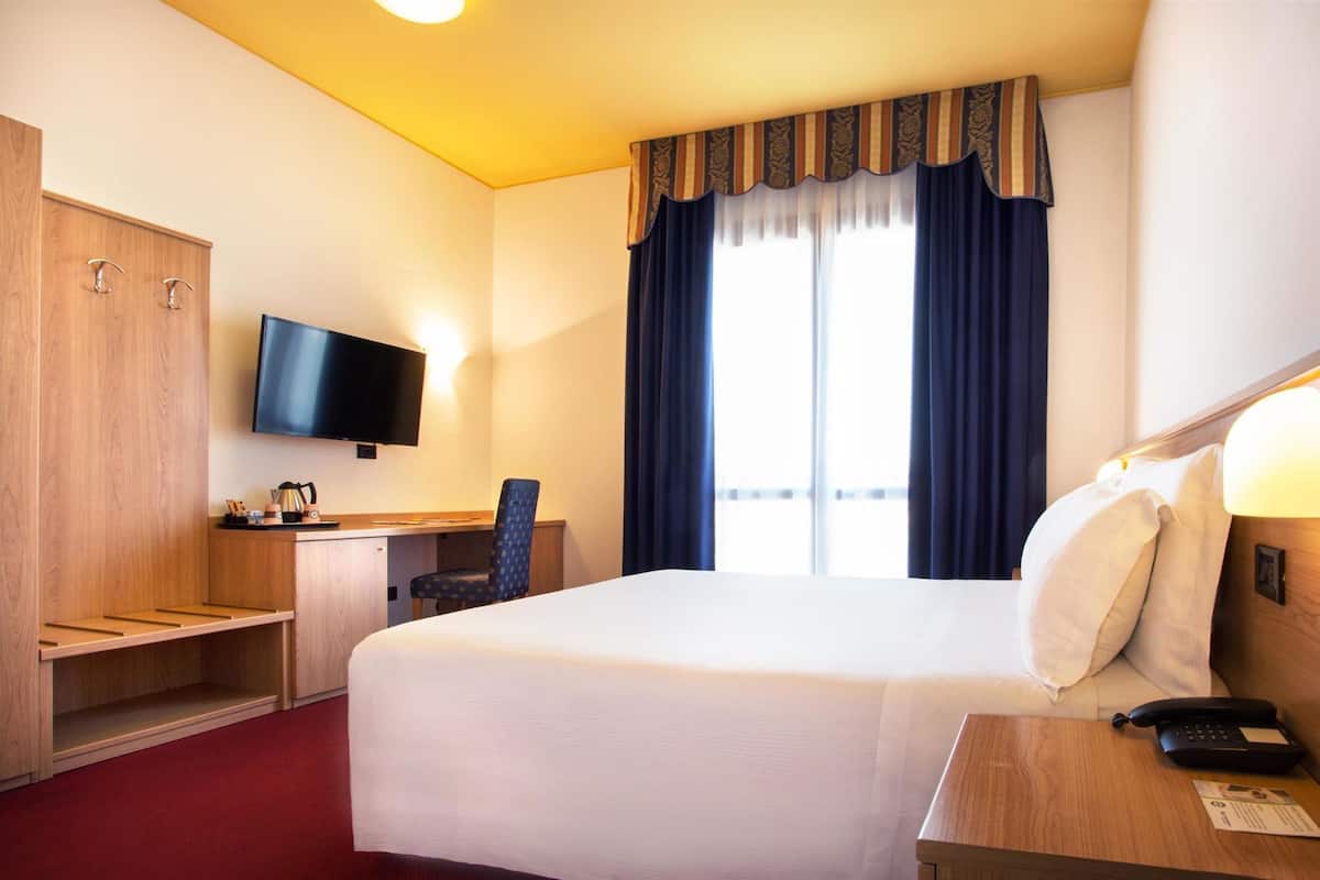 Una habitación de hotel con cama, escritorio, silla, televisor y teléfono.