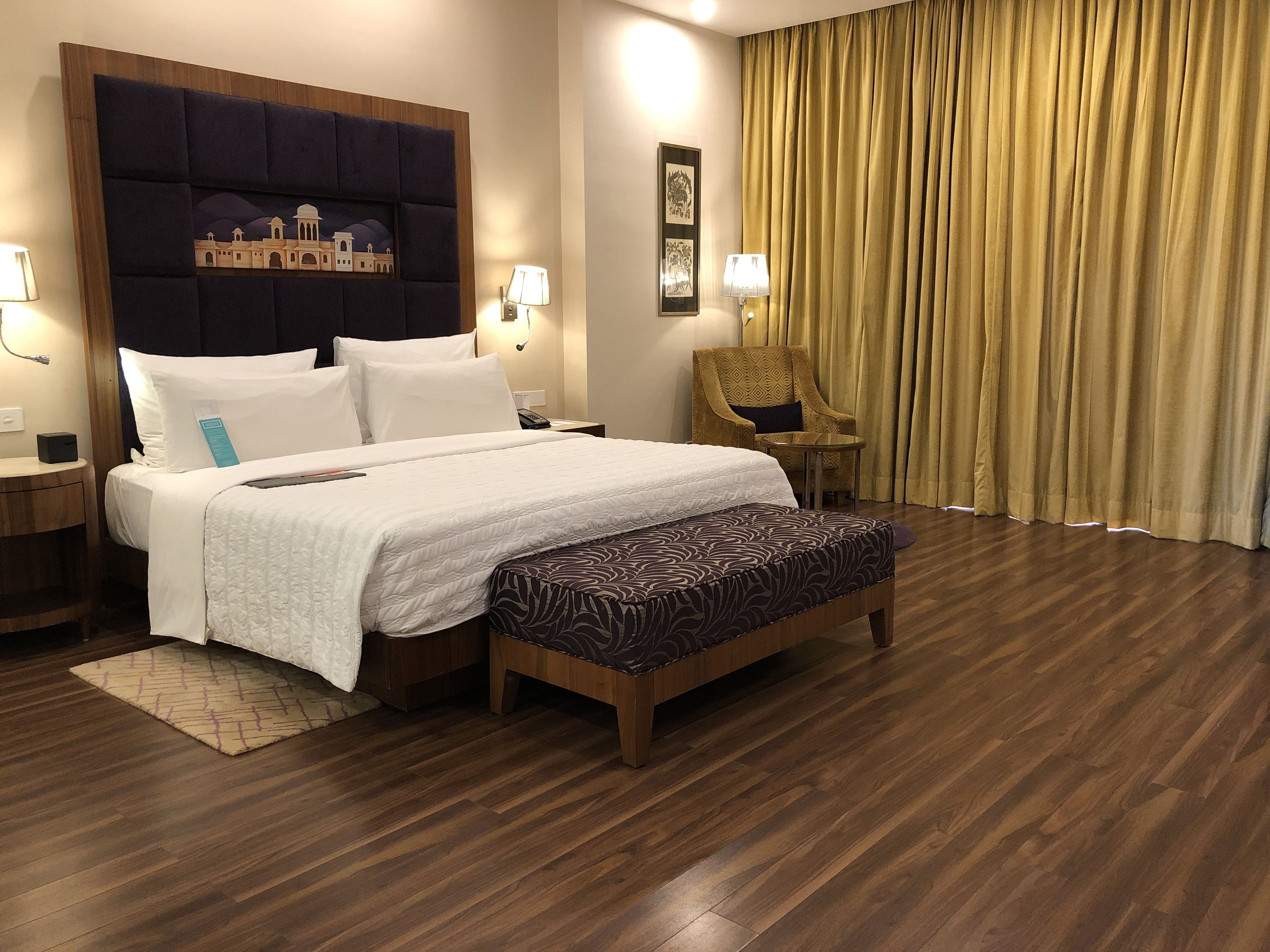 Ein Hotelzimmer mit einem großen Bett, einem Nachttisch, einem Sessel, einem Schreibtisch und einem Vorhang.