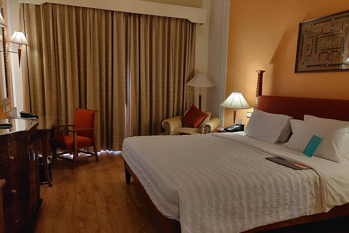 Quarto de hotel com uma cama grande, uma escrivaninha com cadeira, um telefone e uma luminária.