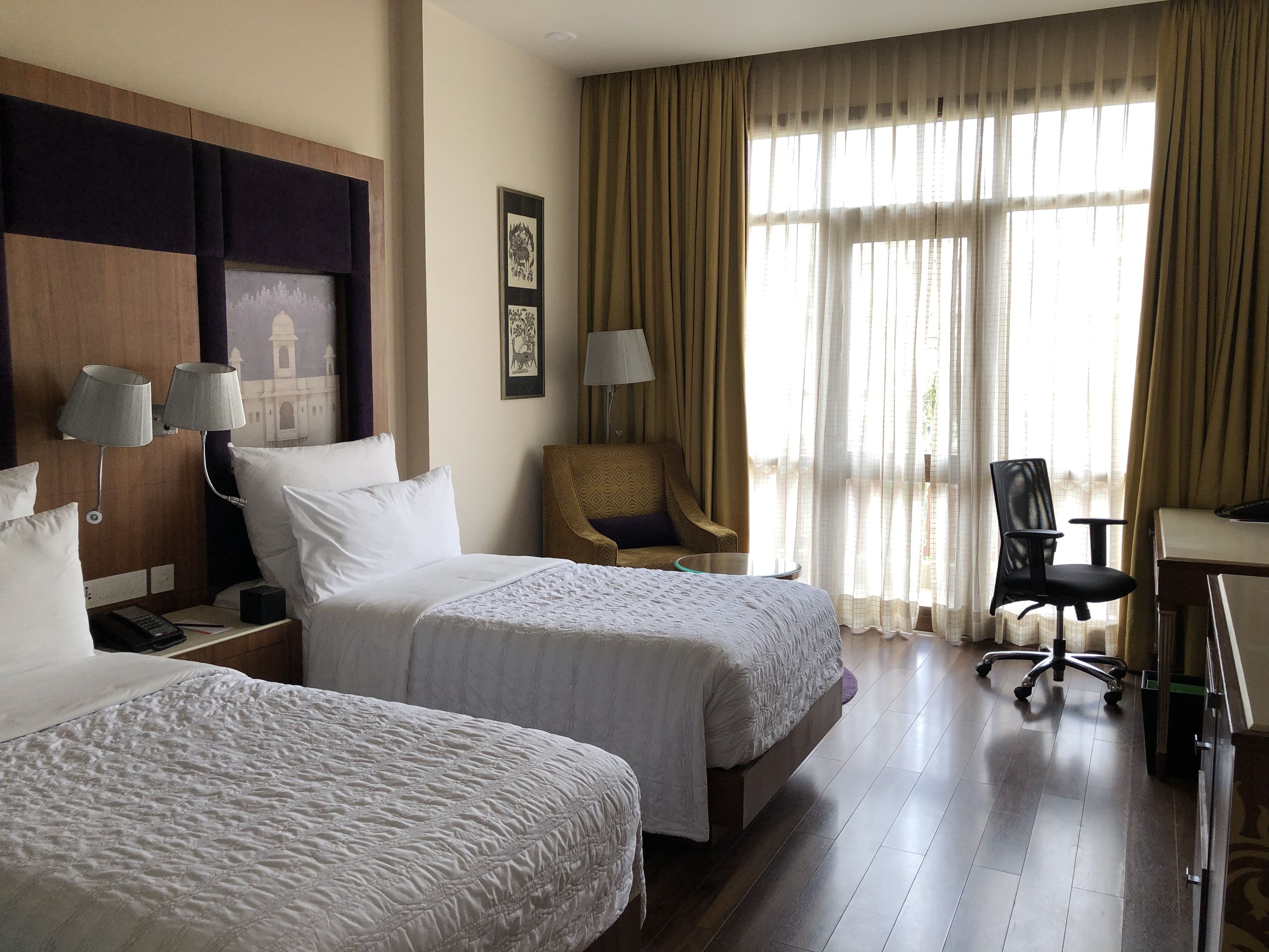 Habitación de hotel con dos camas, un escritorio, una silla y un ventanal con cortinas.