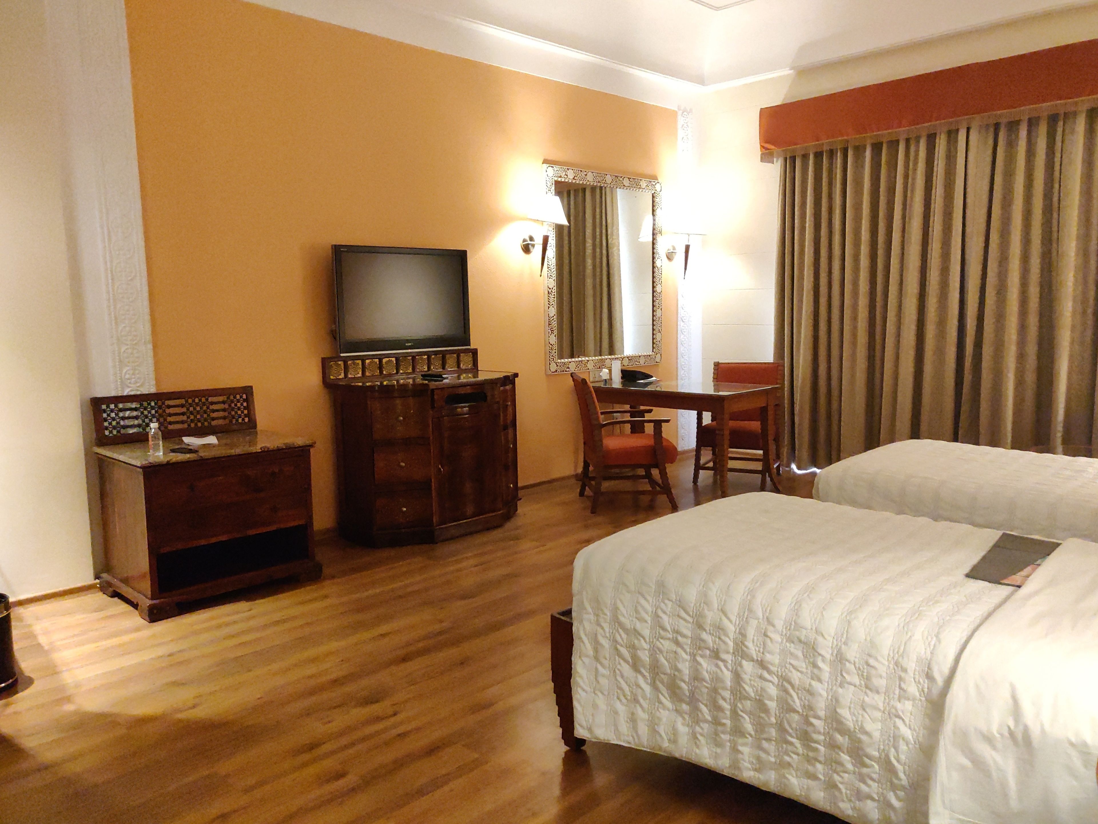 Quarto de hotel com cama, escrivaninha, televisão e espelho.