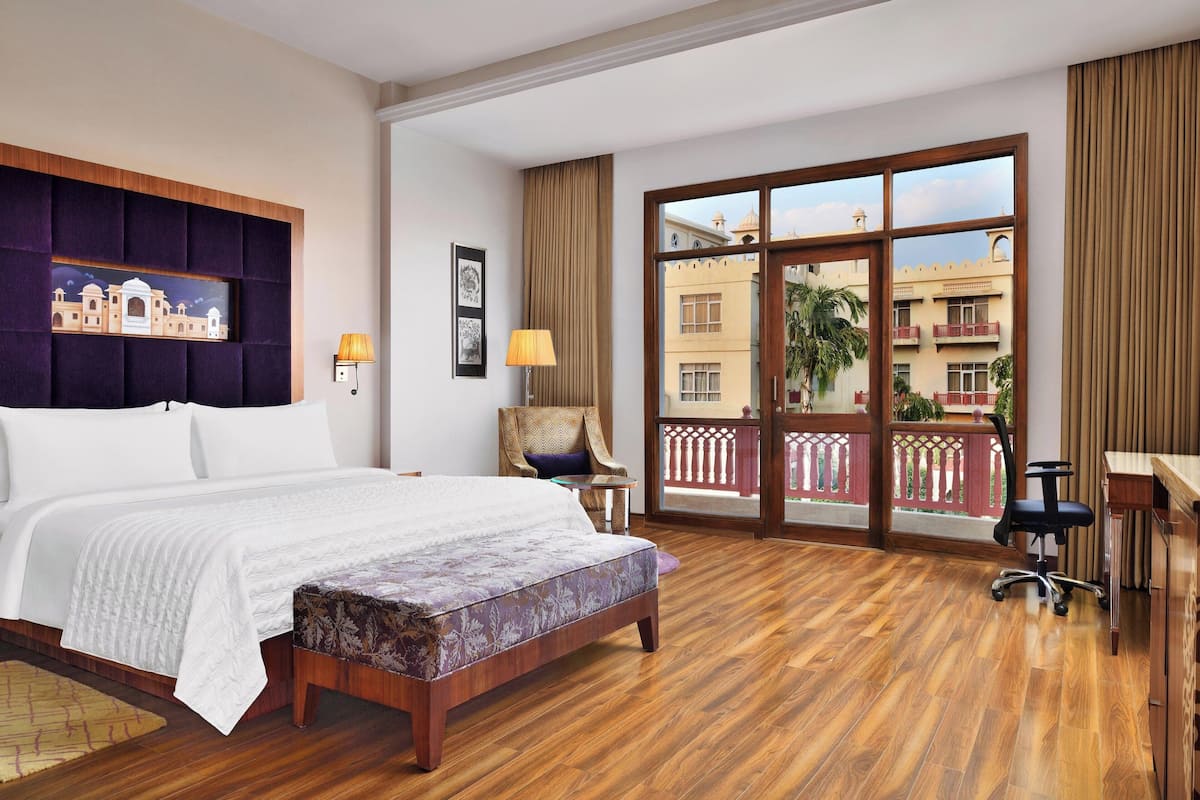 Quarto de hotel com cama grande, escrivaninha, cadeira, janela com vista para edifícios e varanda.