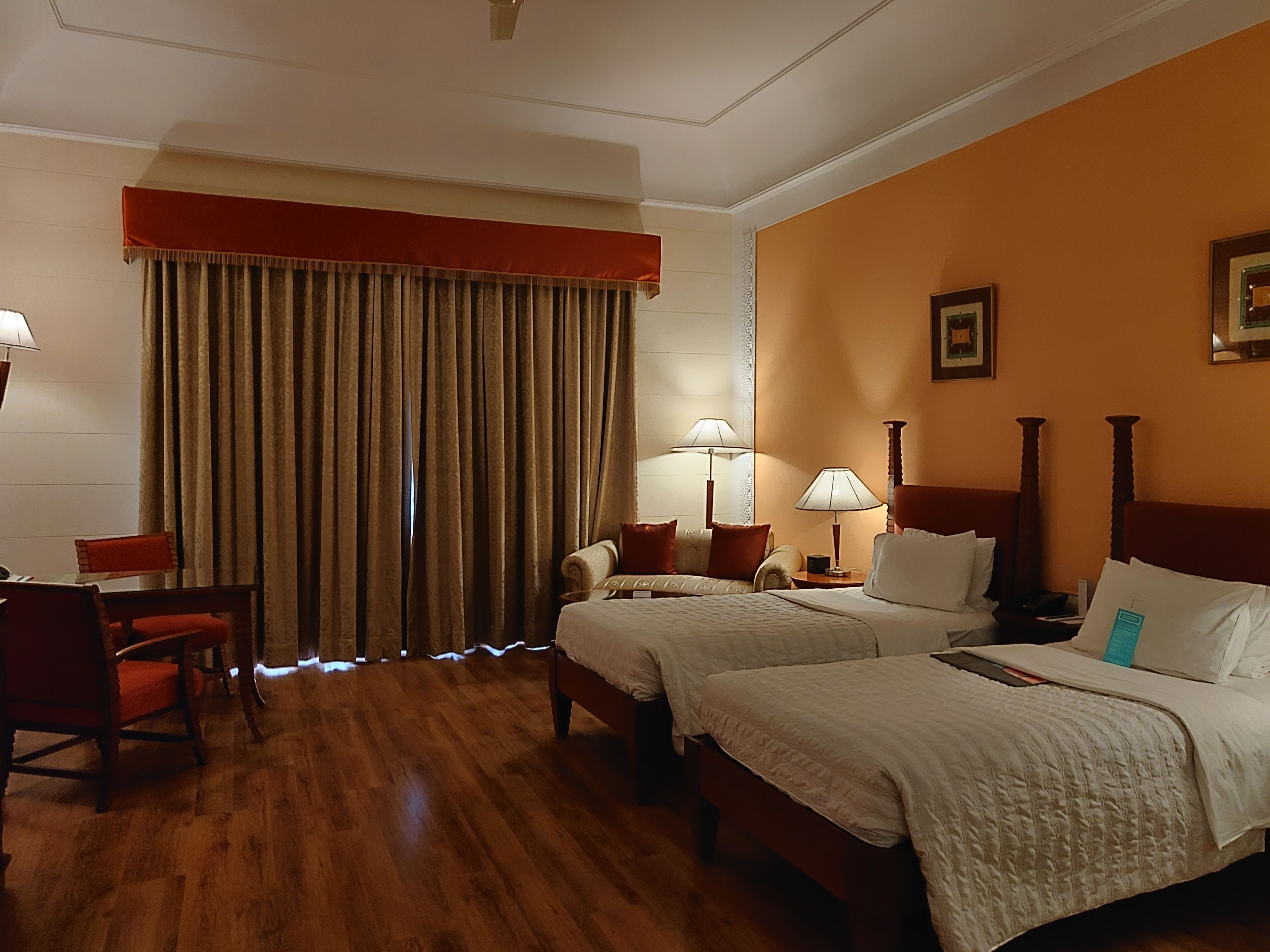 Une chambre d’hôtel avec deux lits, un plancher en bois, un rideau rouge et un bureau avec une chaise.