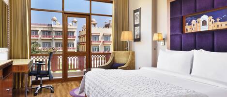 A hotel room with a large window, a bed, a desk, a chair, and a lamp.