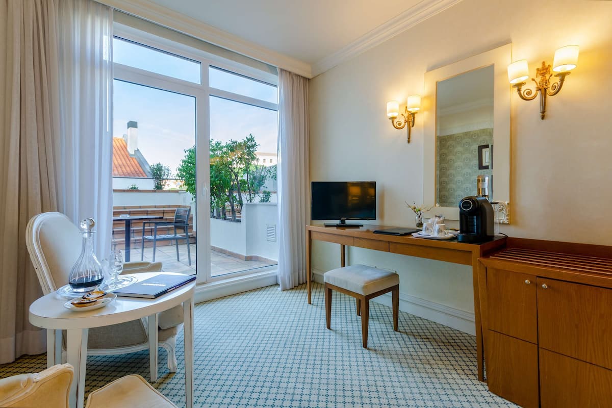 Habitación de hotel con una mesa de comedor, televisor, cafetera y un amplio ventanal con cortinas.