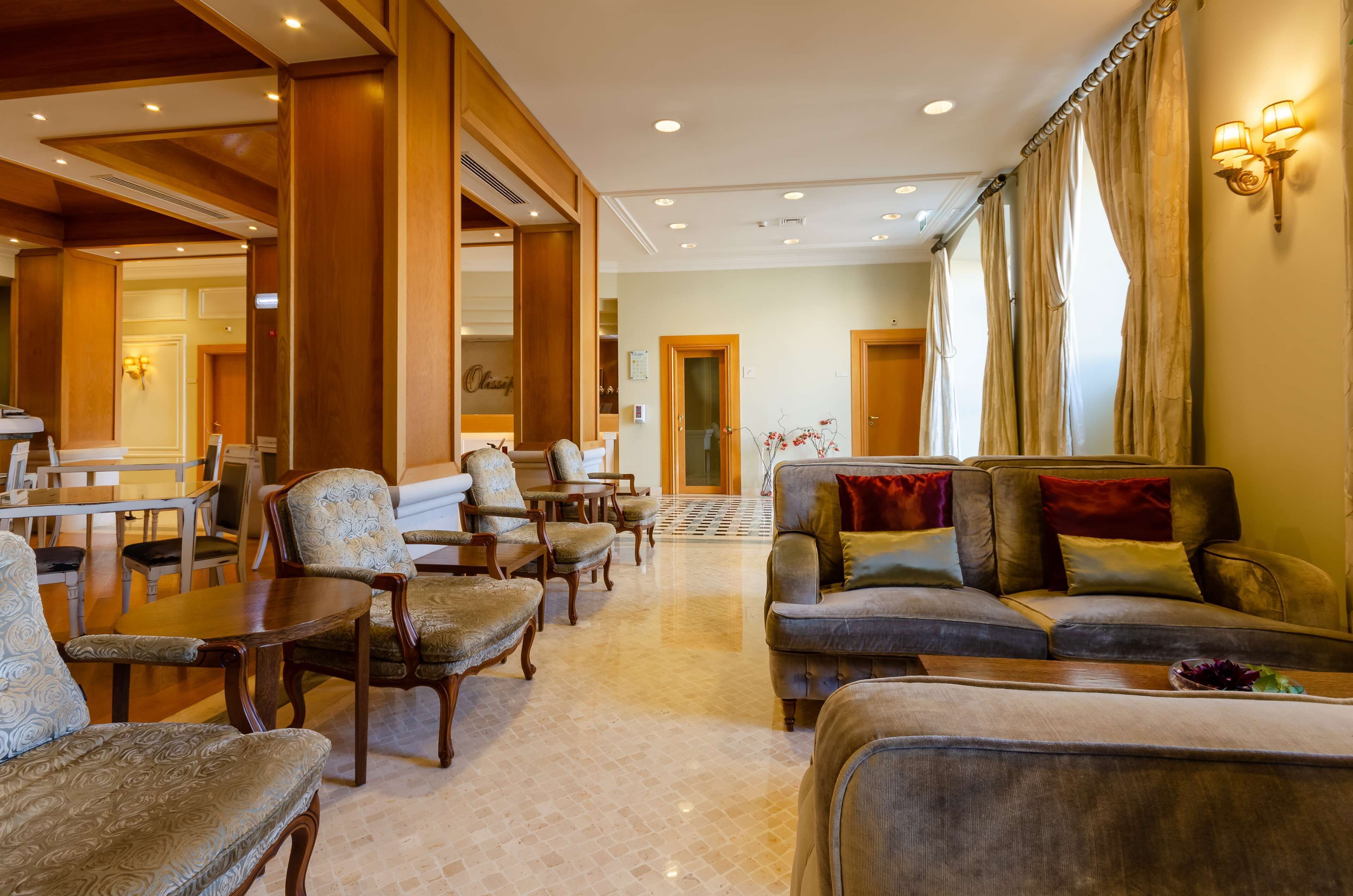 A spacious living area with a sofa, armchairs, and a coffee table. There is a dining area with a table and chairs in the background.