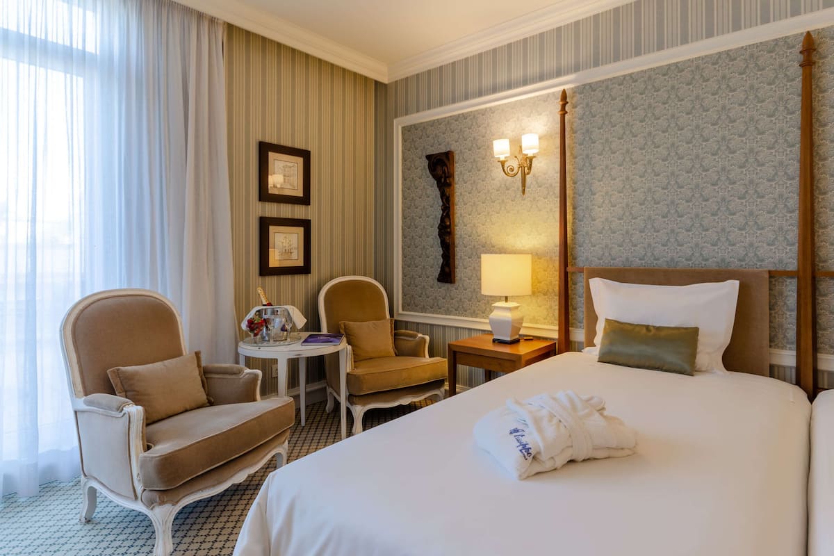 Una habitación de hotel con una cama grande, dos sillones, una mesita con una lámpara e iluminación empotrada en la pared.