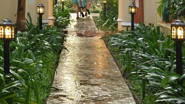 A wet pathway leading to a building with a tiled roof, surrounded by lush greenery and illuminated by lanterns. - Park Inn by Radisson Goa Candolim (Candolim)