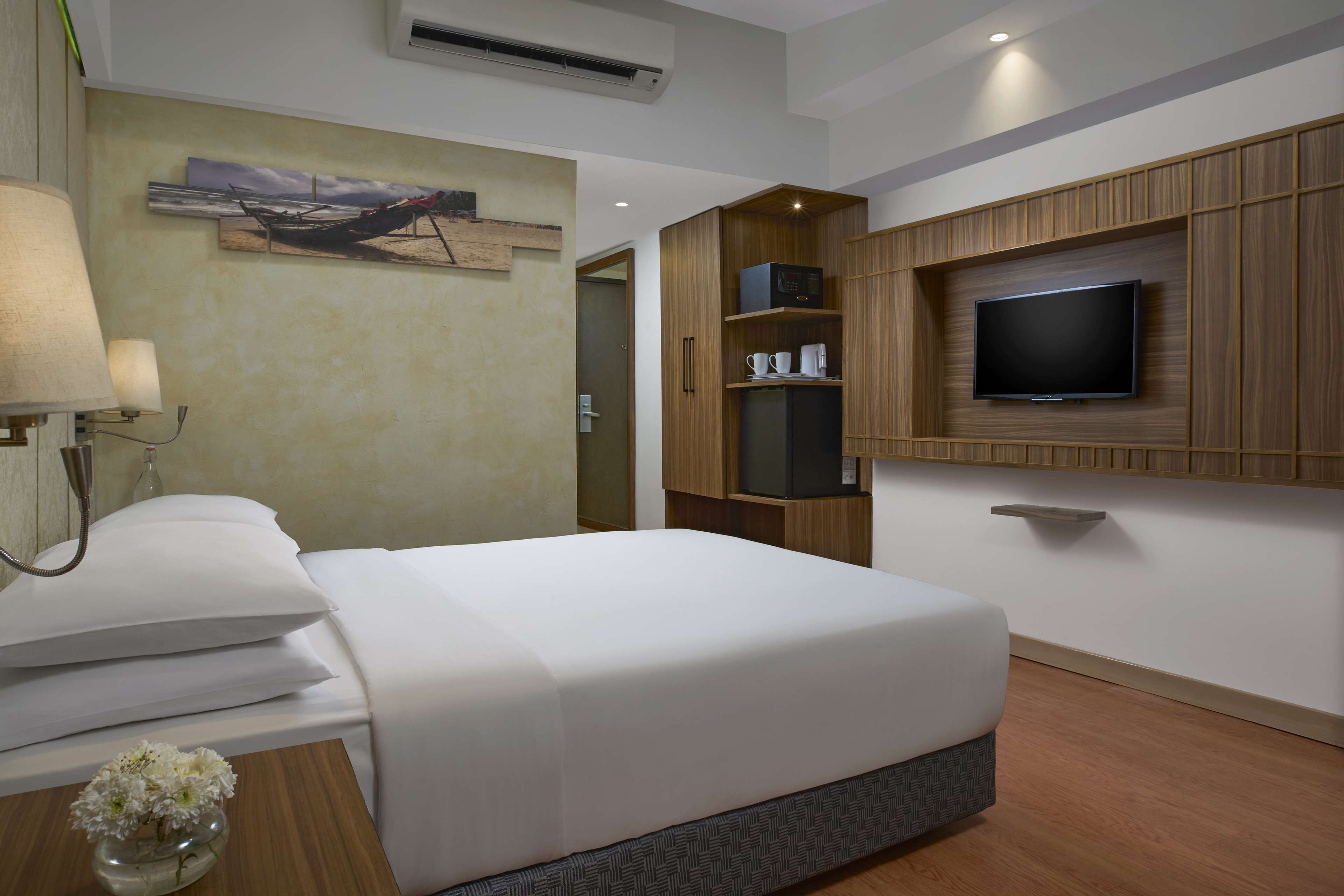 A hotel room with a bed, a TV mounted on the wall, a wooden cabinet, and a painting on the wall.