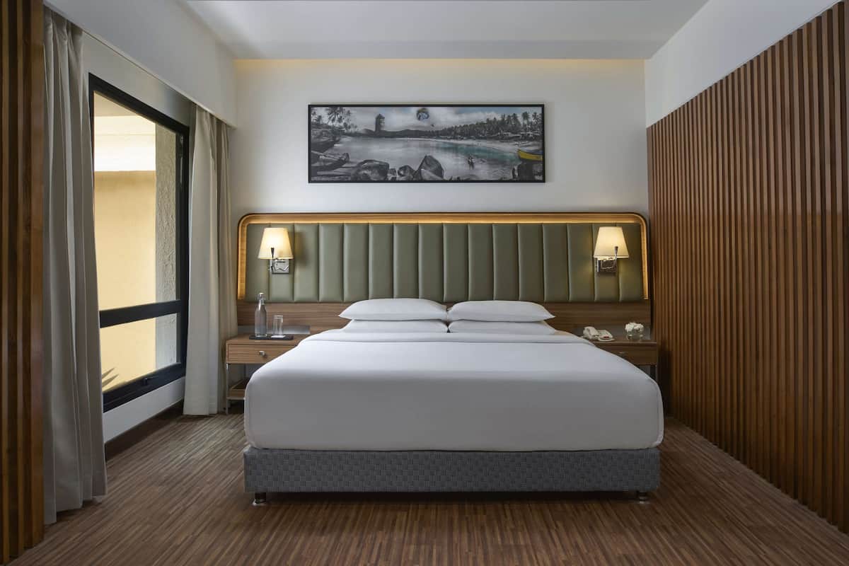 A hotel room with a large bed, two bedside tables, a headboard, a wall-mounted artwork, and a window with curtains.