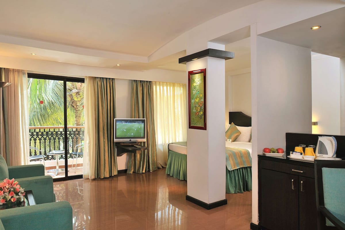 A hotel room with a TV, a sofa, a dining table, a bed, and a balcony with curtains.