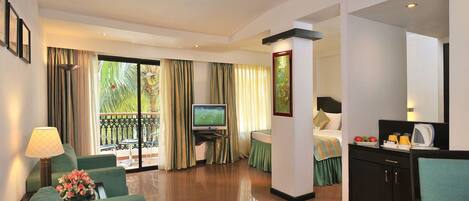A hotel room with a TV, a sofa, a dining table, a bed, and a balcony with curtains.