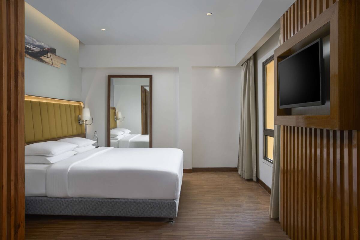 A hotel room with a bed, a television, a mirror, and a wooden paneling design.