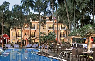 Un hotel con piscina rodeada de sillas de descanso y mesas de comedor, palmeras y una zona de bar.