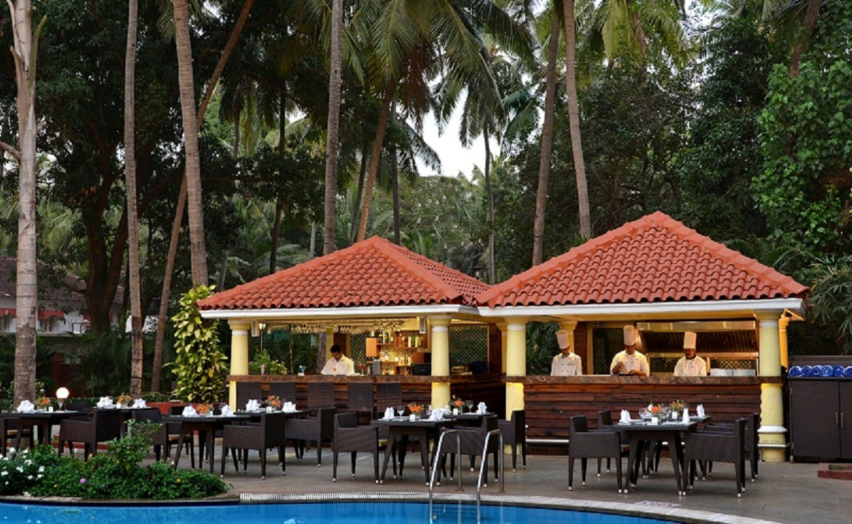 An outdoor restaurant with a pool, surrounded by palm trees.