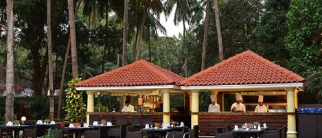 An outdoor restaurant with a pool, surrounded by palm trees.