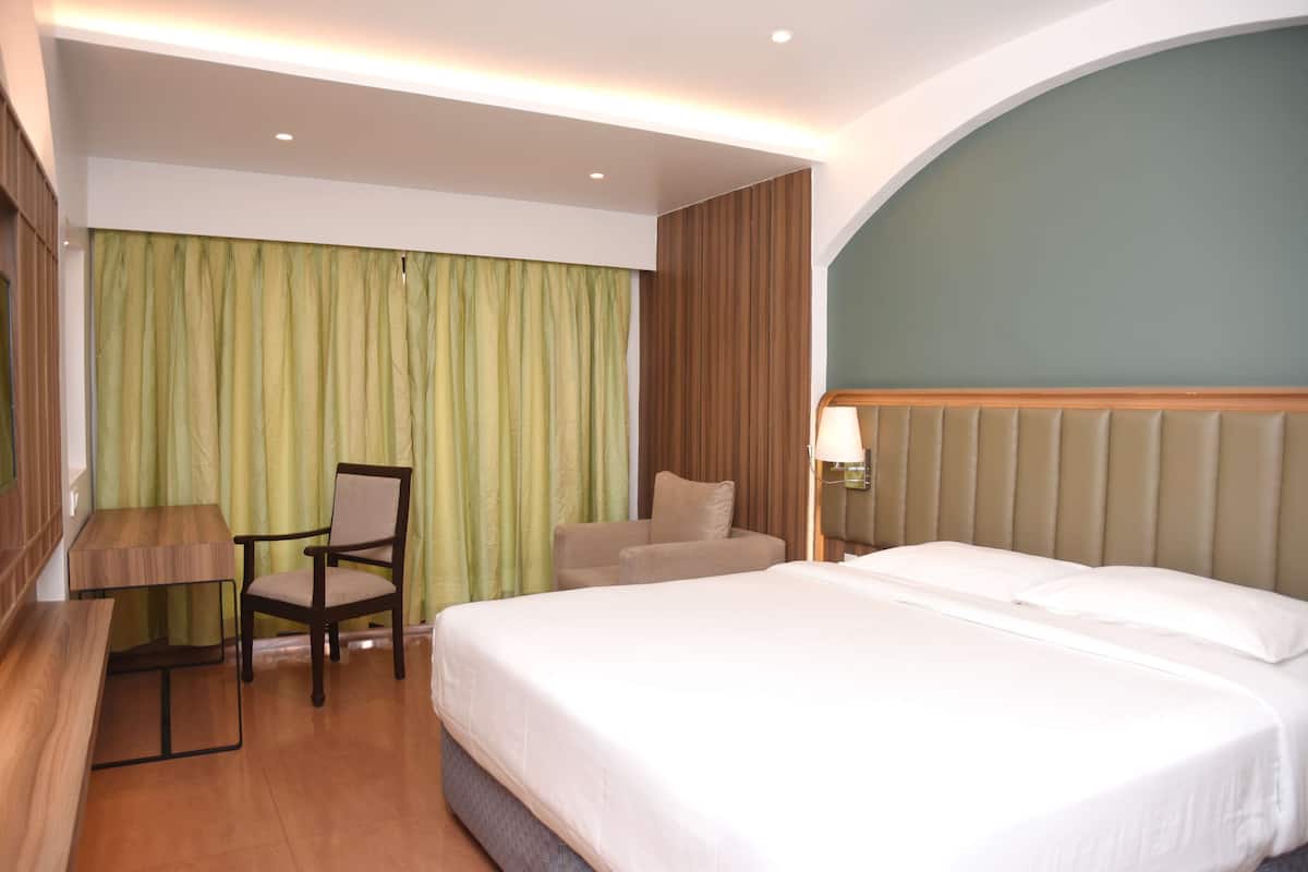 A hotel room with a large bed, a desk, a chair, and a lamp.