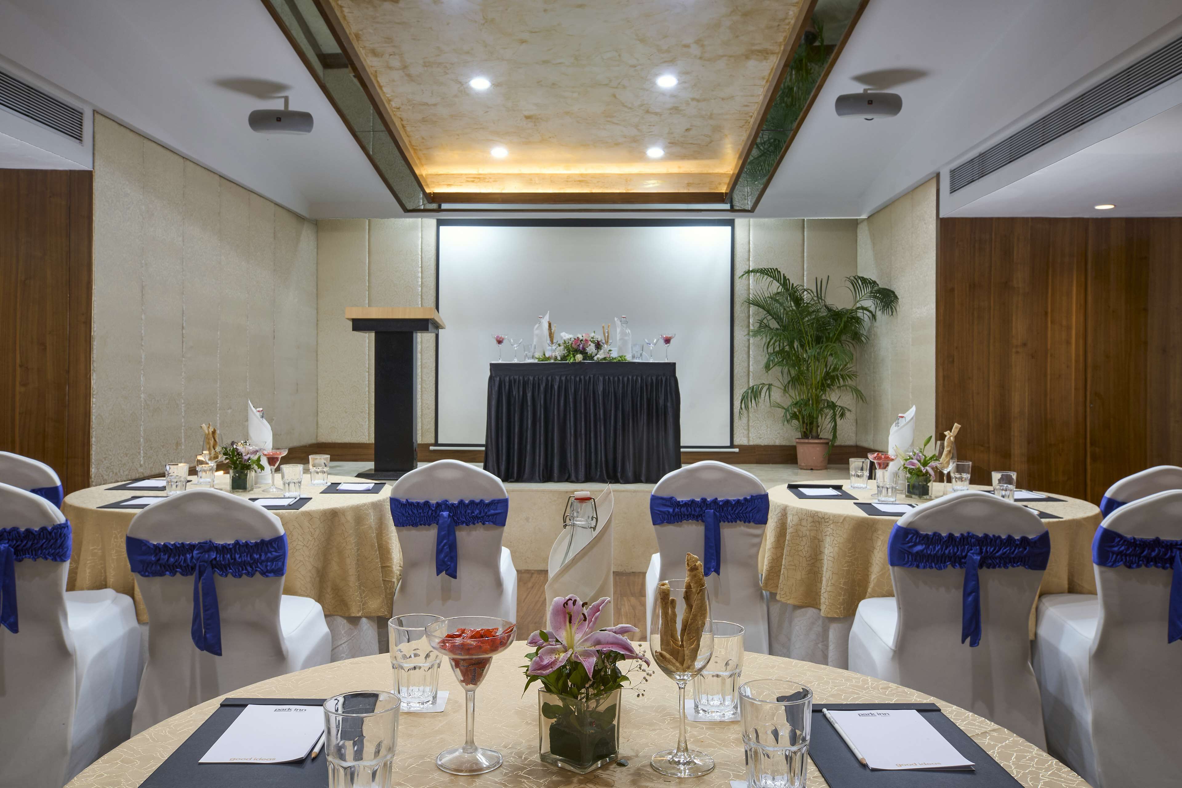 Un salón de conferencias con mesas redondas, sillas blancas con cintas azules y un atril al frente.