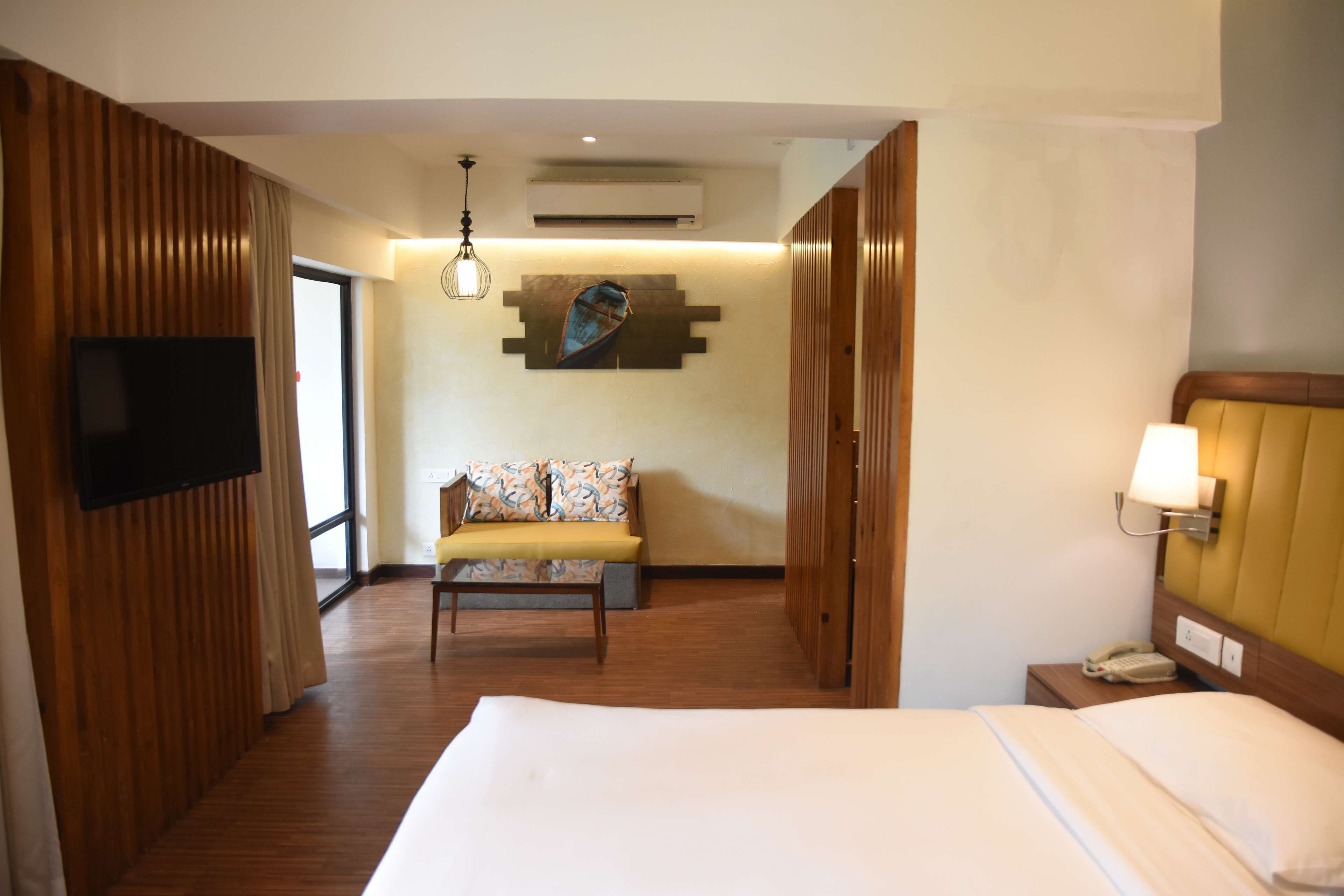 A hotel room with a bed, a sofa, a TV, a phone, and a wall-mounted light fixture.