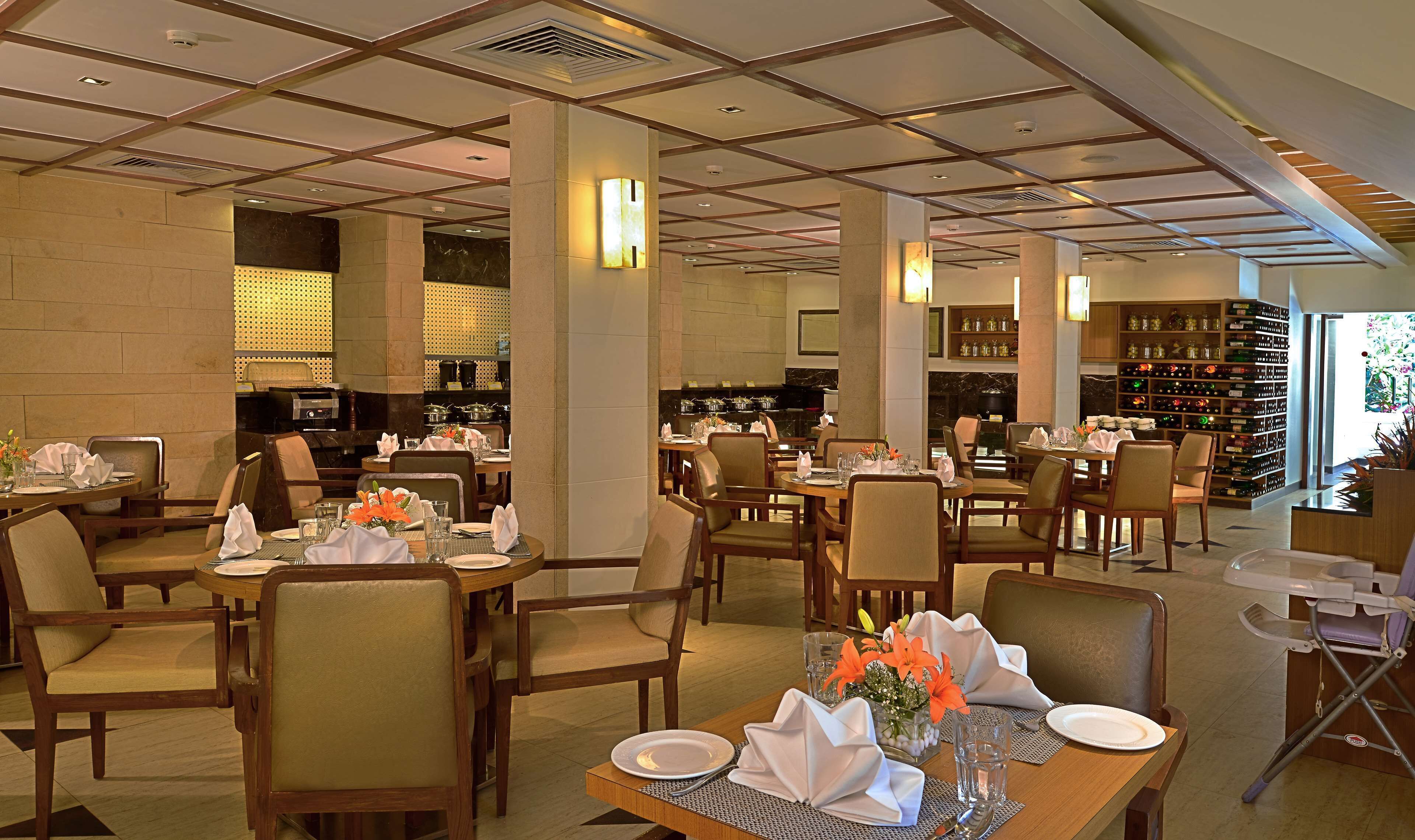 A well-lit restaurant with multiple dining tables, chairs, and a visible kitchen area.