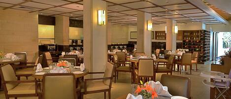 A well-lit restaurant with multiple dining tables, chairs, and a visible kitchen area.
