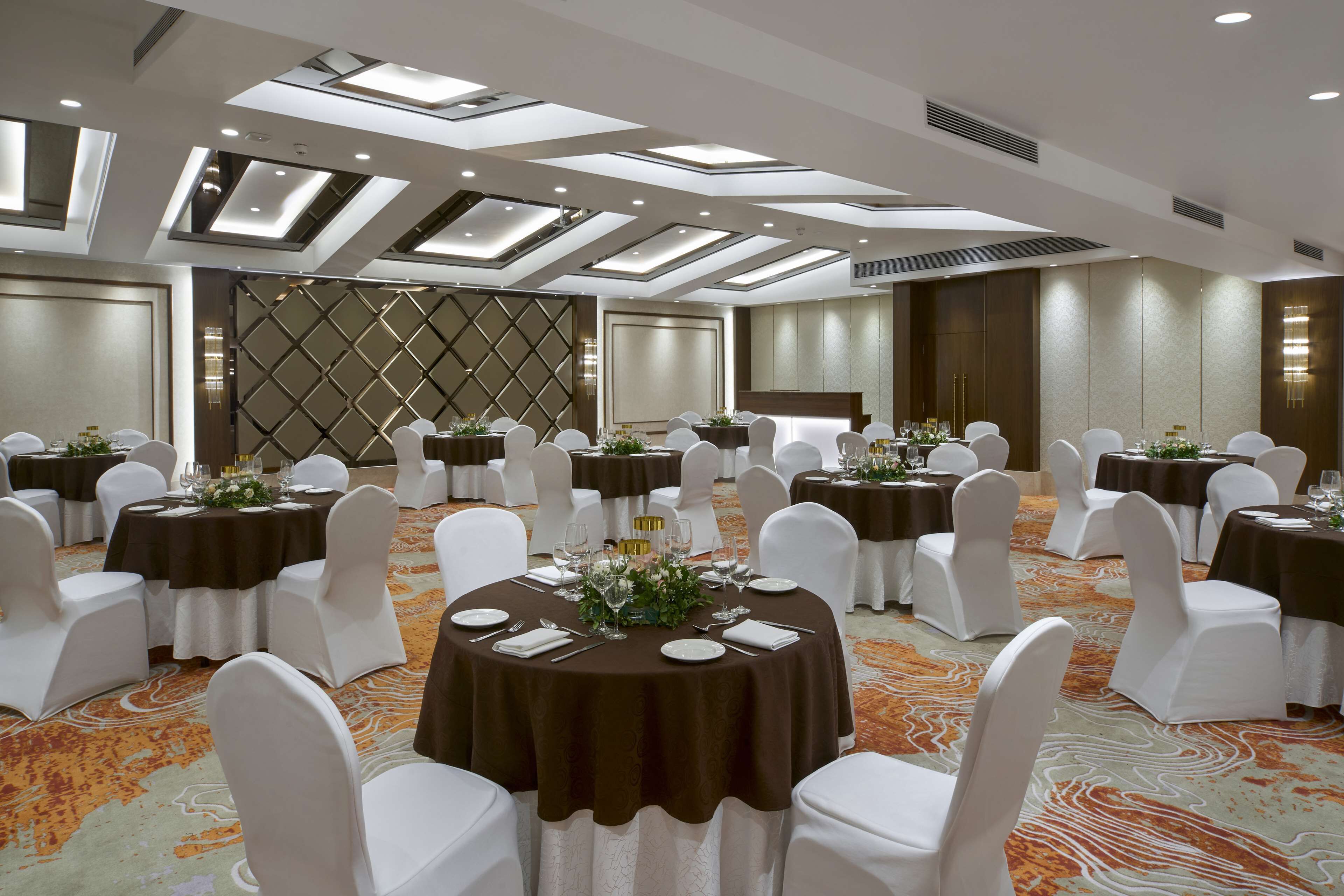 Un salón de conferencias con mesas redondas, sillas blancas y alfombra estampada.