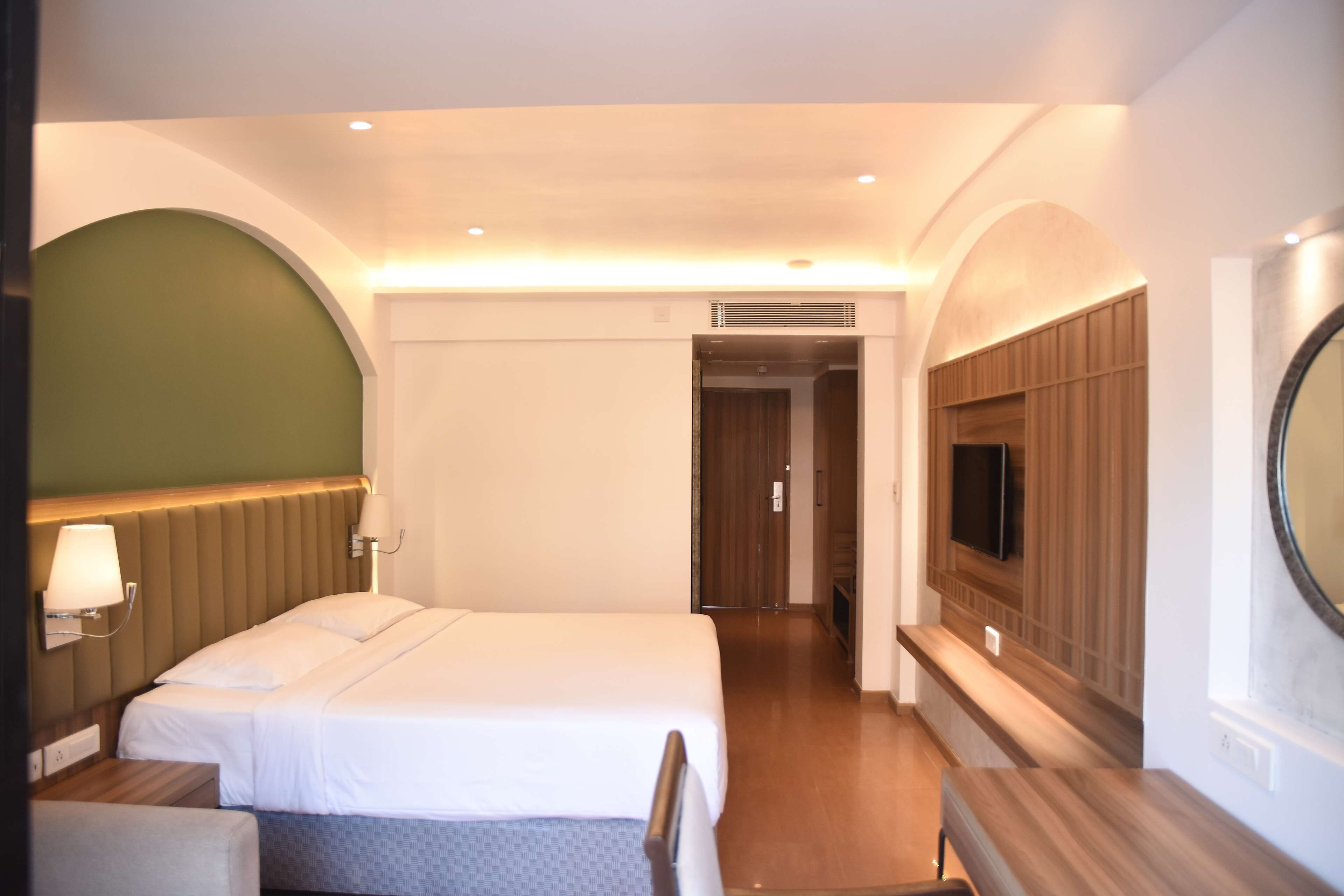 Una camera d'albergo con un letto, un comodino, una lampada, una TV e uno specchio.