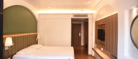 A hotel room with a bed, bedside table, lamp, TV, and a mirror.