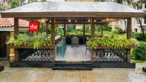 A covered outdoor seating area with wooden tables and chairs, surrounded by lush greenery and a tiled floor. - Park Inn by Radisson Goa Candolim (Candolim)