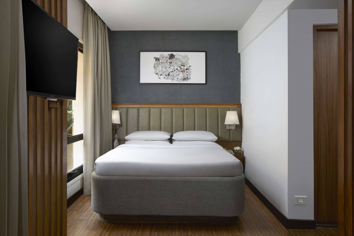 A hotel room with a large bed, a flat-screen TV, a framed artwork on the wall, and a wooden headboard.