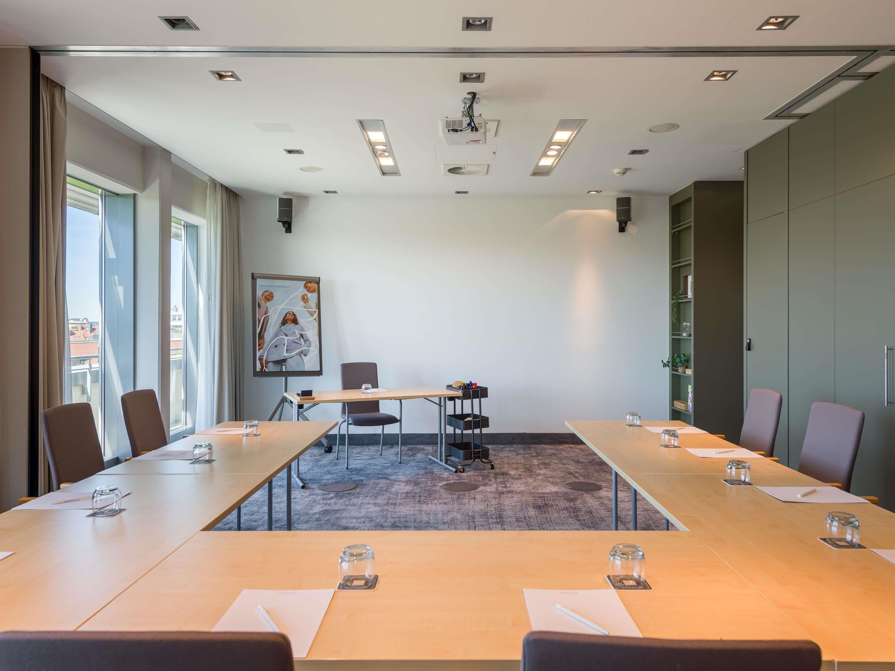 A conference room with a long table, chairs, a projector screen, and a large window with curtains.