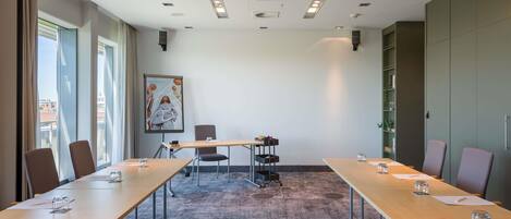Un salón de conferencias con una larga mesa, sillas, una pantalla de proyector y un amplio ventanal con cortinas.
