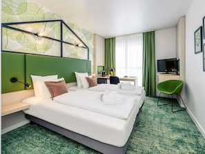 A hotel room with a large bed, a desk, a chair, a TV, and a green carpet. - Mercure Hotel Hannover Mitte (Hannover)